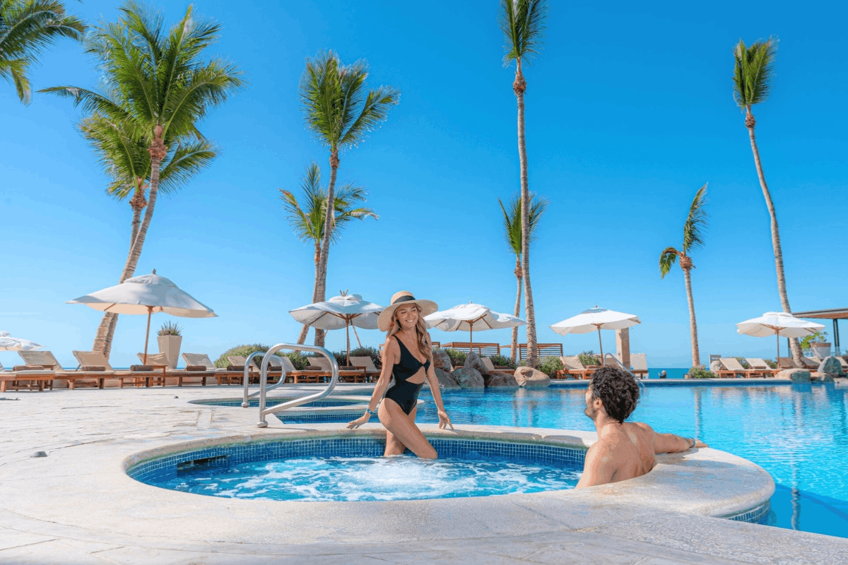 Albercas de Krystal Grand Los Cabos frente al mar con jacuzzi, palmeras y espacios para relajarse bajo el sol.